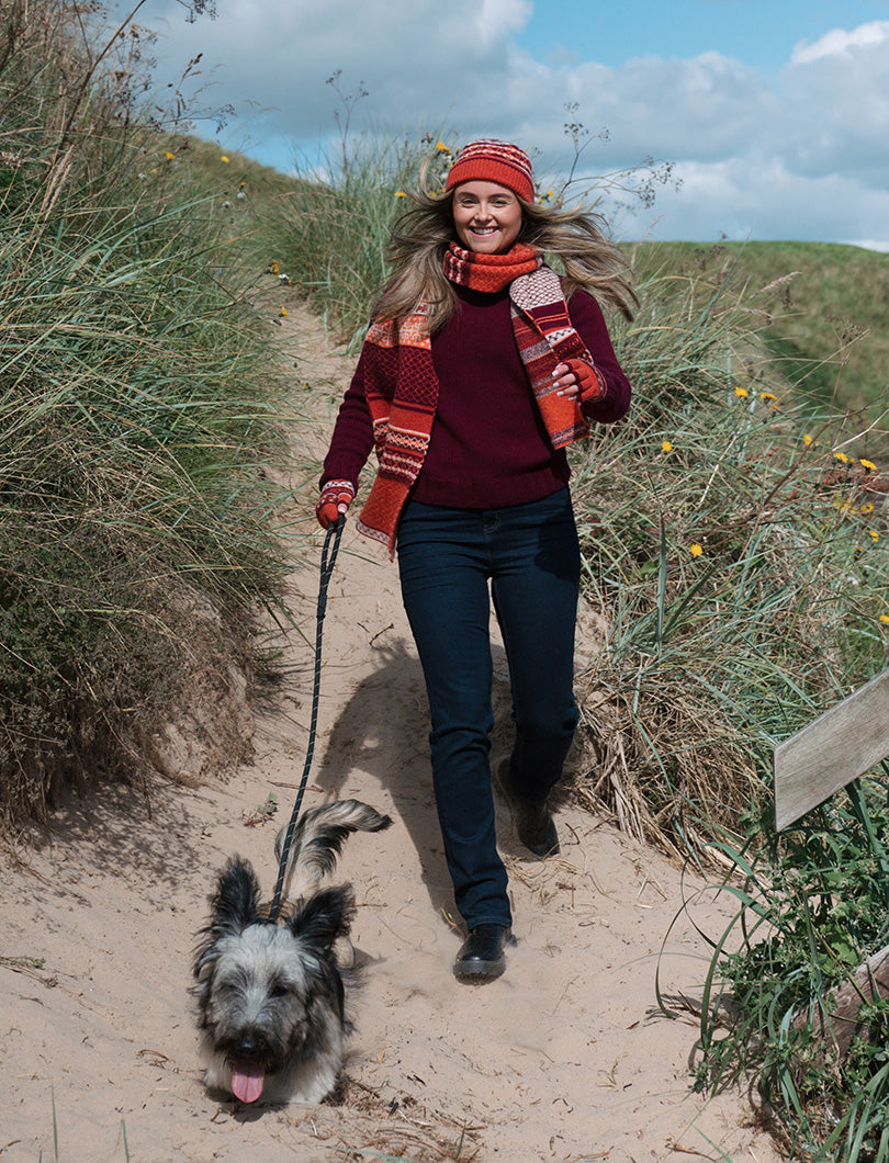 Girl wearing an orange fair isle scarf walking a Skye Terrier